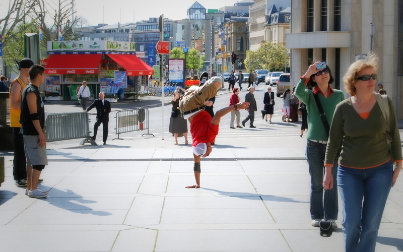 4 - A public square with people walking and a street performer breakdancing in the center